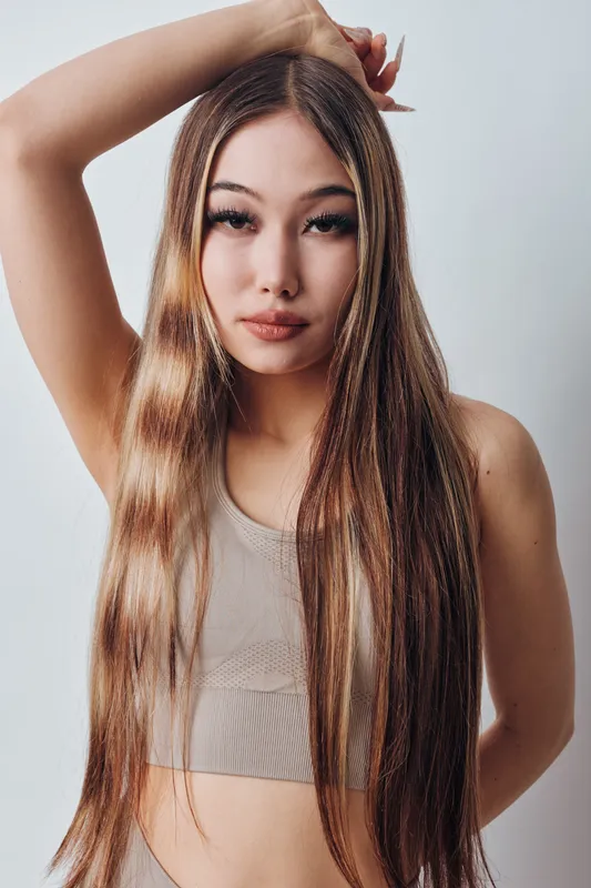 Young woman with long straight hair posing in neutral top against a light background. Closeup portrait with natural makeup and expressive eyes in studio lighting.
