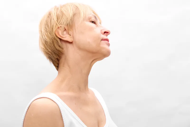 Senior woman portrait in profile, calm expression with short blonde hair, wearing a white top on a clean white background, concept of wellness and healthy aging.