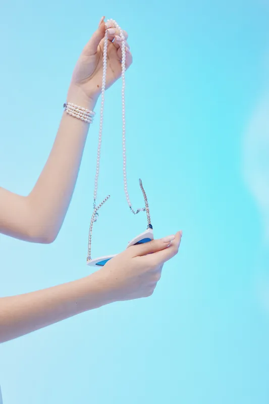 Close-up of a woman holding a pearl necklace and a small purse against a blue background. Concept of beauty, fashion, and elegant accessories for stylish women.