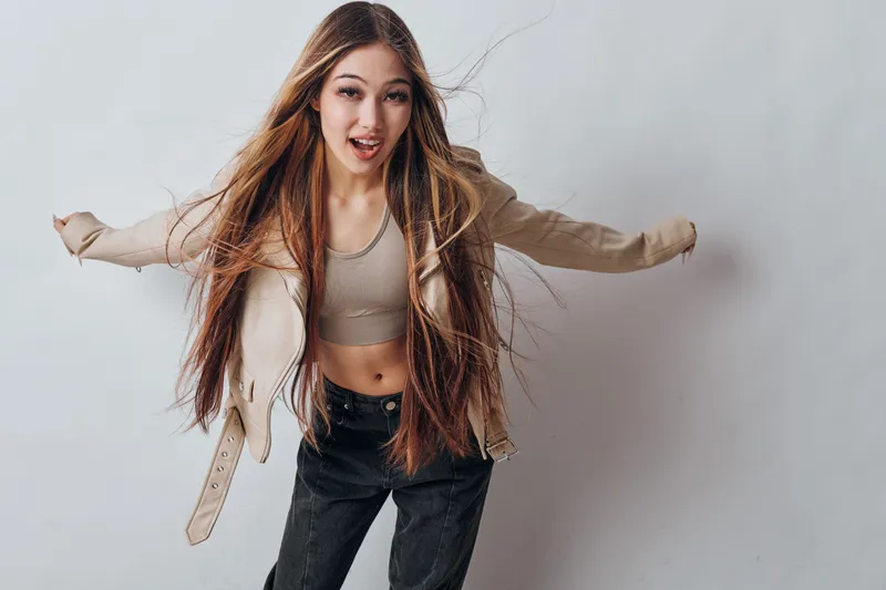 Young woman with long hair wearing casual jacket and crop top posing with arms open against white background in studio. Fashion, portrait and lifestyle with dynamic expression.