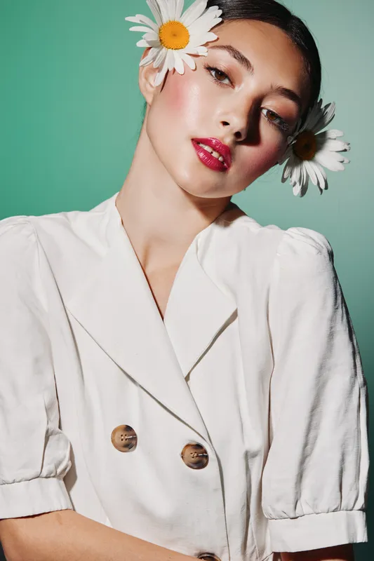 Fashion stylist poses in white fashionable blouse with shoulder puff, natural makeup, pink luminous lips, perfect skin on green seamless background, showcasing beauty and creative concept.