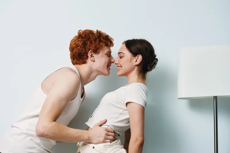 Couple, love, kiss and smiling with affection and intimacy at home in casual clothes for romance and relationships. Young man and woman with happy moment indoors near lamp.