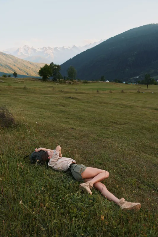 Young woman lifestyle relaxing lying on grass in open field with mountains in background enjoying nature and peaceful outdoor environment on sunny day.