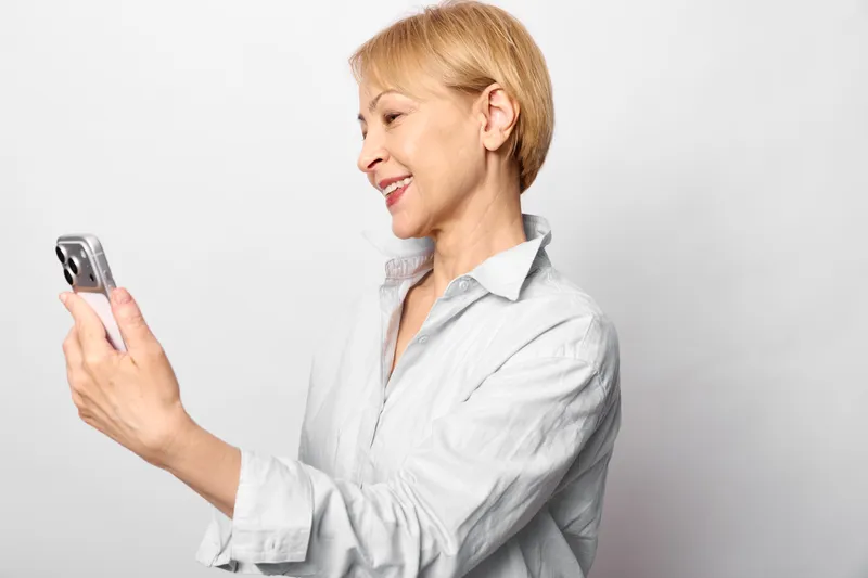 Woman smartphone profile blonde portrait female holding communication, woman using touchscreen phone in side view, smiling calmly, isolated on white background