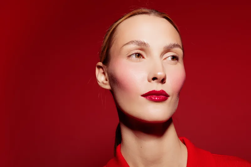 Portrait of a woman with red lipstick and smooth skin on red background. Concept of beauty, makeup, fashion, and confident female model with natural light and vibrant colors.