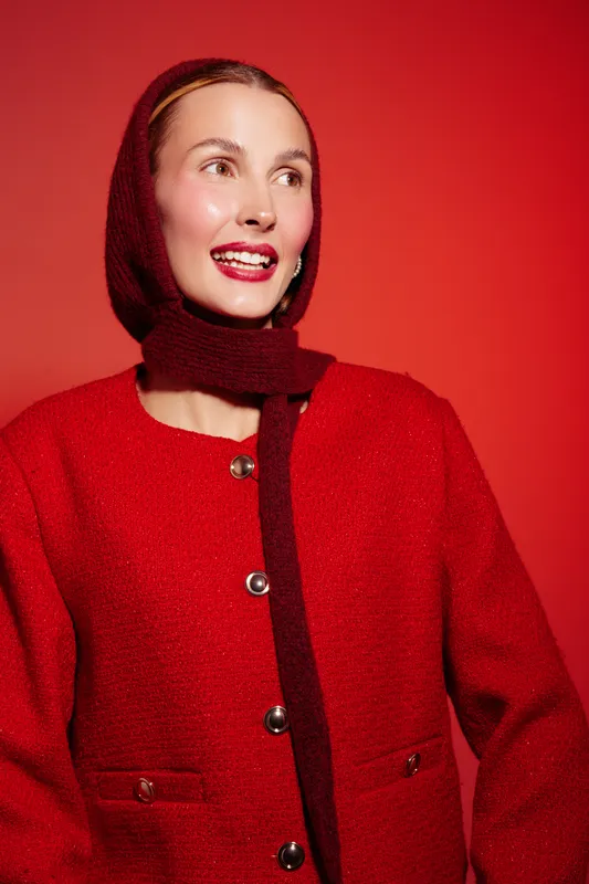 Smiling woman in red wool coat and matching scarf looks aside on red background. Studio portrait with bright lighting and warm tones. Concept of fashion, winter style, and happiness.