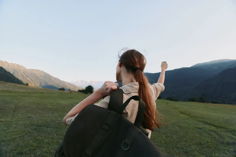 Young woman with long hair carries a large backpack while hiking in a wide open mountain valley during a clear day, enjoying the outdoor adventure and freedom.
