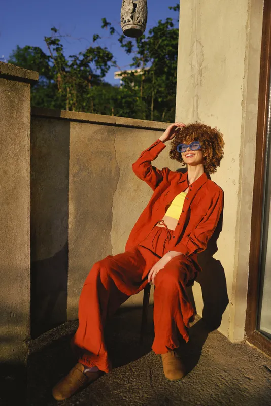Portrait of a woman in an orange suit posing on a sunlit rooftop, expressing confident lifestyle and fashion in an urban setting with warm tones and modern vibe
