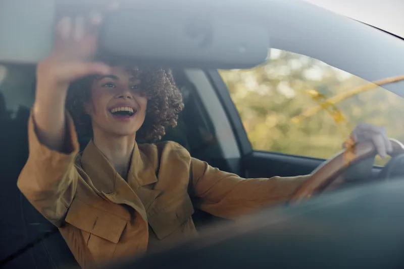 A joyful woman drives a car with a bright smile, retro film color tones evoke a warm lifestyle moment, capturing carefree energy, spontaneous laughter, open road scenery, sunlight on hair, and a