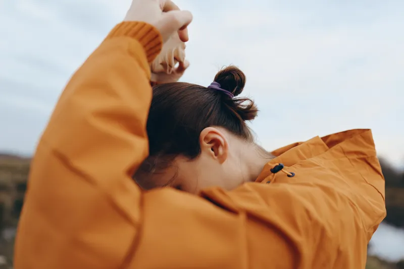 Mother and child share an embrace outdoors, woman in orange jacket holding close, soft sky background, caring lifestyle moment, tenderness and love, closeup