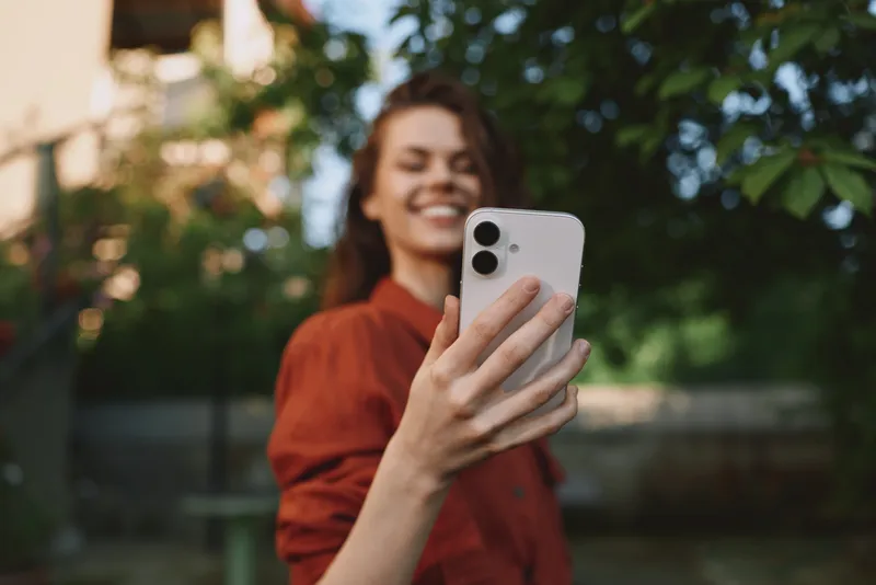Vibrant woman lifestyle outdoor selfie smiling casual portrait smartphone sunshine nature with greenery backdrop, relaxed mood, authentic moment, park setting, soft breeze, golden hour, joyful vibe