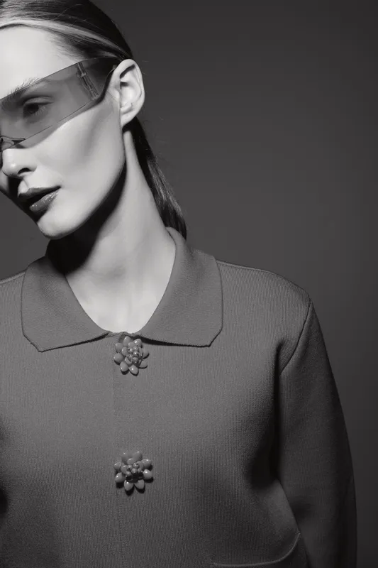 Young white woman with pale skin wearing futuristic visor and textured jacket in black and white studio portrait.