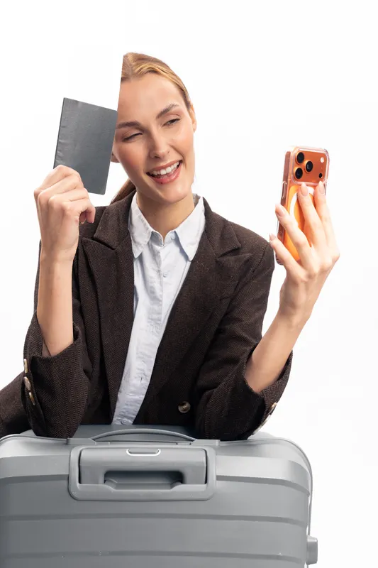 Young woman with suitcase holds passport and takes selfie on smartphone. Concept of travel, vacation, trip preparation, and happiness during journey planning.