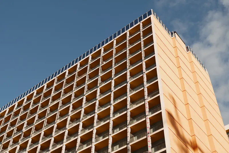 Unfinished orange facade of a tall building under construction, exposed steel frame, grid pattern, strong perspective, architectural details, bright sky, industrial mood