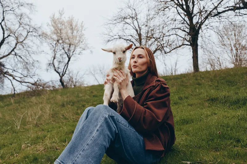 Portrait of a woman holding a small goat on a hillside outdoors in a natural setting Warm calm mood conveys companionship nature and rural lifestyle with soft gentle lighting