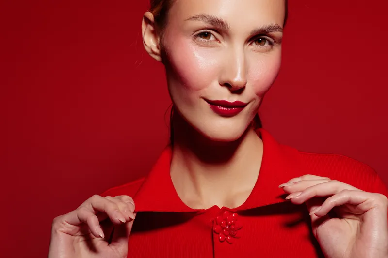Close-up portrait of confident woman with red lipstick and red outfit against red background. Concept of fashion, beauty, elegance, and bold style with vibrant monochrome tones.