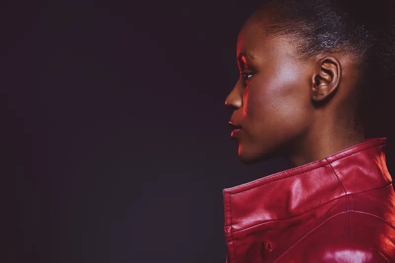 Profile of an African woman with dark skin wearing a red leather jacket on a dark background. Concept of fashion, beauty, and confident female portrait in studio lighting.