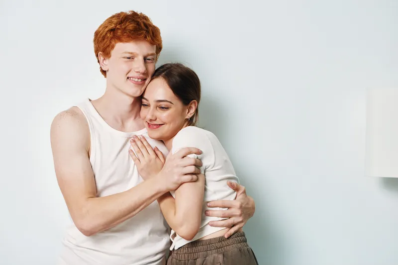 Young couple hugging indoors with happiness, smiling together in casual clothes, showing affection and love with close embrace and relaxed atmosphere.
