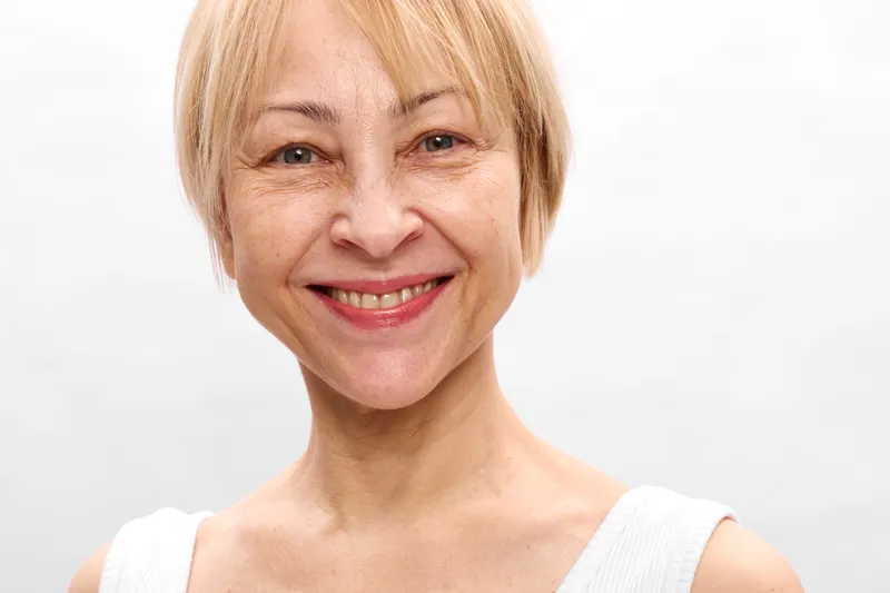 Woman smile senior face skin beauty selfcare portrait, blonde woman close up headshot in bright studio, white background, warm lighting, skincare wellness.