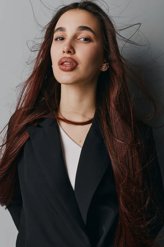 Portrait of confident young woman with long hair wearing black blazer and white top against gray background. Fashion, beauty, model, studio, casual, elegance, style, female, confident.
