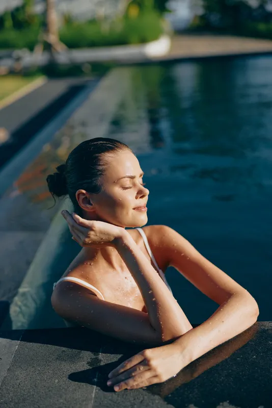 Young woman enjoys relaxing in outdoor swimming pool sunlight on face eyes closed peaceful moment wellness lifestyle summer activity.