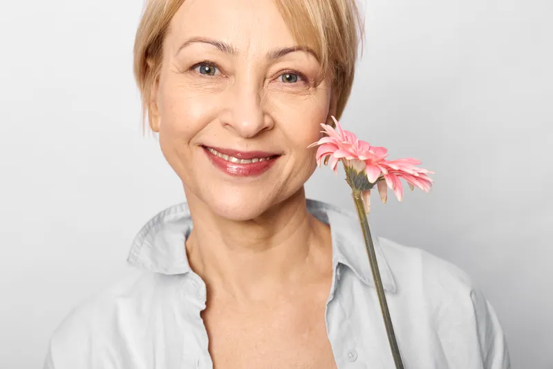 Woman nurse smile holding pink gerbera flower, studio portrait closeup, gentle caring compassion, healthcare support and kindness for wellness, white background spring mood