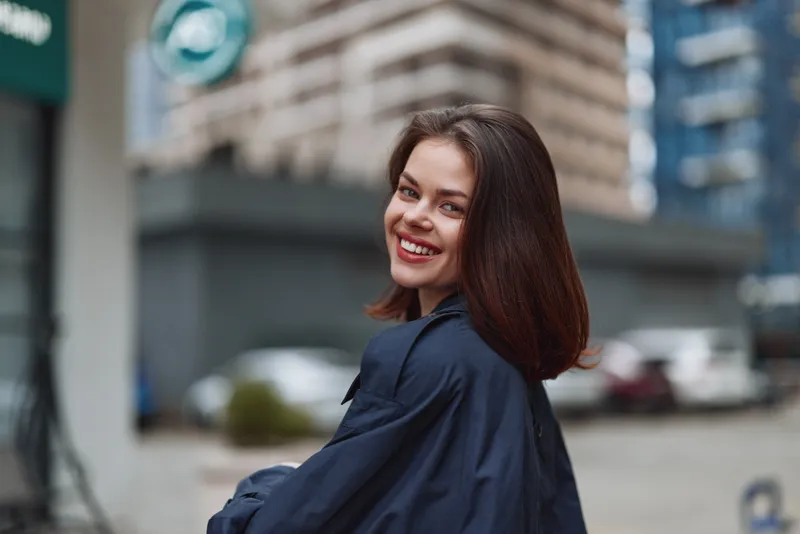 Smiling woman with shoulder length brunette hair in an urban street setting. Casual outfit and city vibe convey confidence, style, and everyday life.