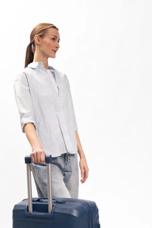 Young woman in casual white shirt and jeans holds suitcase handle, looking sideways. Concept for travel, journey, vacation, or business trip with minimalistic white background.