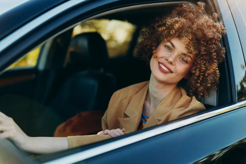 Vibrant woman in a car, smile through the window, a sunny moment that captures lifestyle and retro film color, a candid portrait of relaxed confidence and cheerful ease