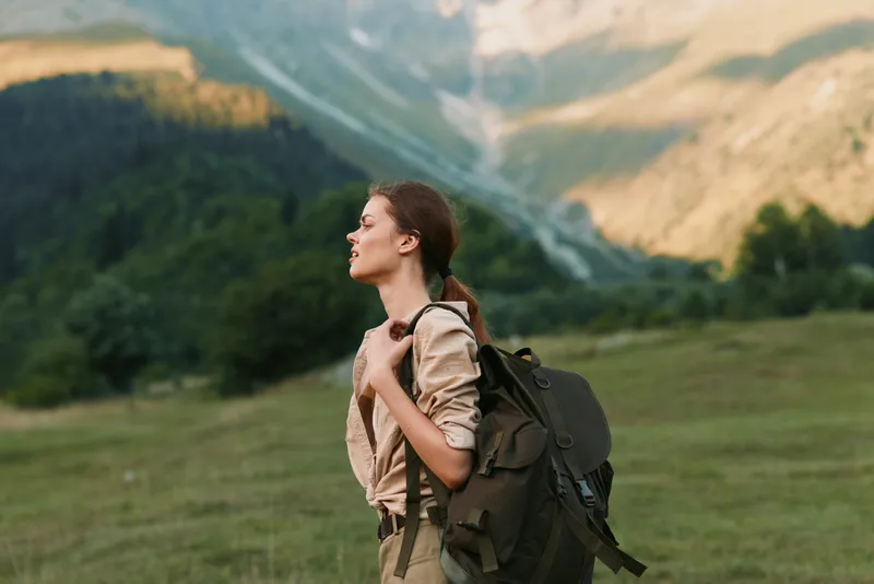 Young woman with a backpack enjoys a peaceful moment while hiking in a mountainous landscape during a sunny day.