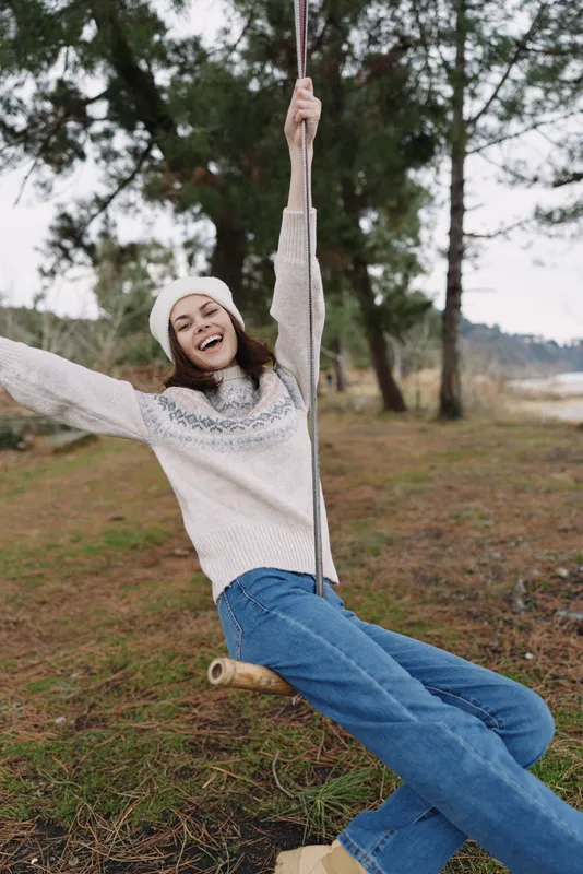 outdoor swing girl laughing carefree playground nature park breeze horizon sunlight candid happiness motion youth sweater jeans forest scenery smile moment innocence landscape grass sky relaxation