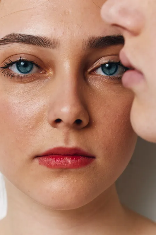 Woman with blue eyes and natural skin closeup looking at camera with red lips and well defined eyebrows, detailed face showing texture and expression with white background.