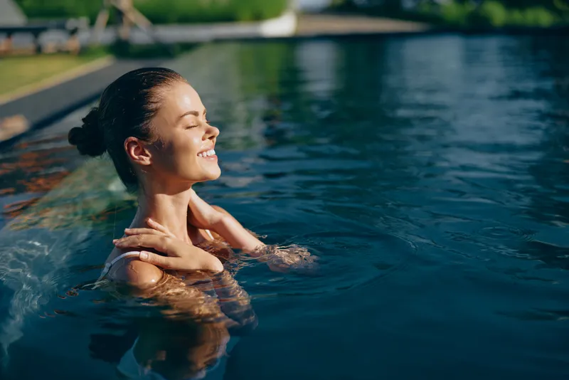 Relaxed woman enjoys a pool on a sunny day, floating with gentle ease, soaking warmth and daylight in a carefree outdoor water scene, presenting a simple lifestyle moment of wellness and tranquility.