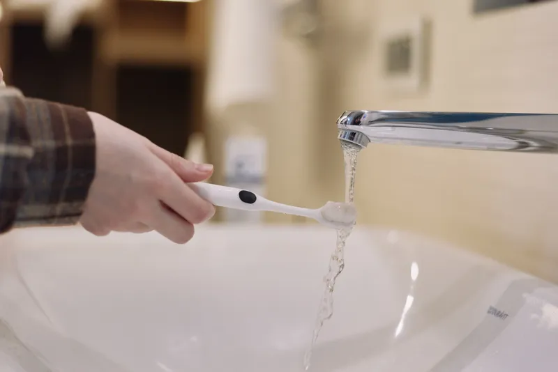 Toothbrush under running water in a bathroom sink, close up of routine hygiene and dental care as a hand rinses and prepares for daily oral health and fresh breath.