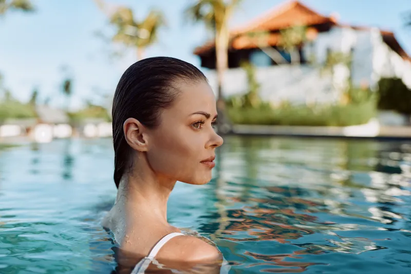 A woman relaxes in a clear pool, the outdoor scene showcasing leisure and self care as water surrounds her, capturing summer serenity by the pool.