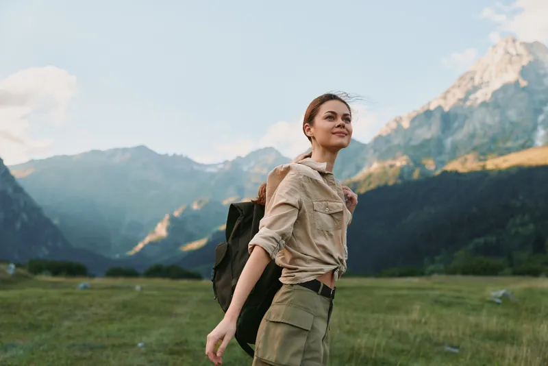 Young woman traveler hiking in mountains with backpack enjoys fresh air and nature landscape during outdoor adventure lifestyle in sunny day.