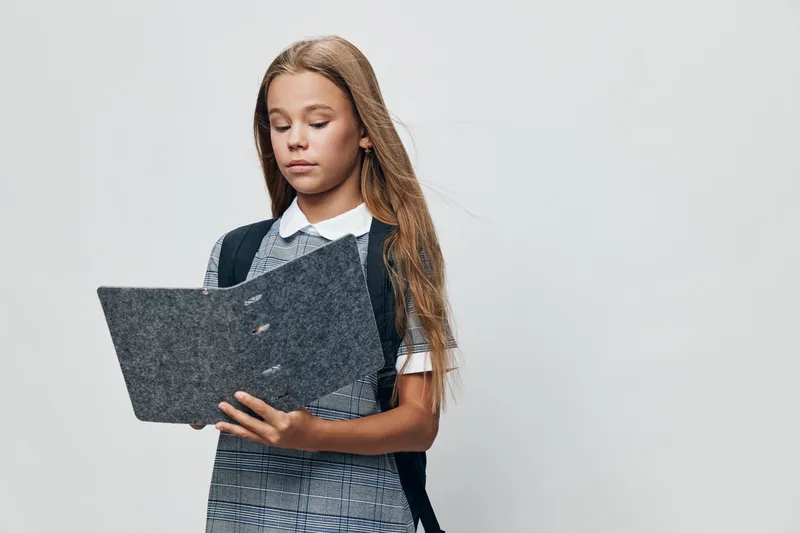 Girl student reading folder with school uniform and backpack on white background for education, learning and study concept with serious expression in classroom or academy.