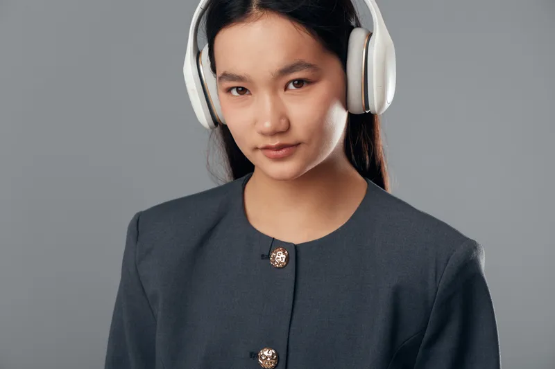 Young woman wearing headphones and dark jacket looks confidently at camera with slight smile on gray background for technology music communication concept.