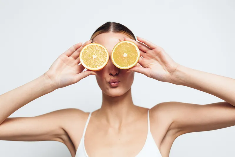Woman, orange, slices, citrus, vitamin, health, beauty, wellness, spa, skincare concept, studio portrait with fruit held over eyes, hands framing mock glasses on clean white background