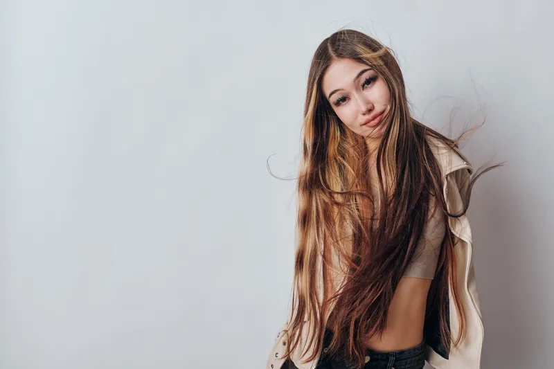 Young woman with long hair wearing casual clothes posing and smiling with head tilt on neutral background studio. Lifestyle, beauty, fashion and confidence with natural look.