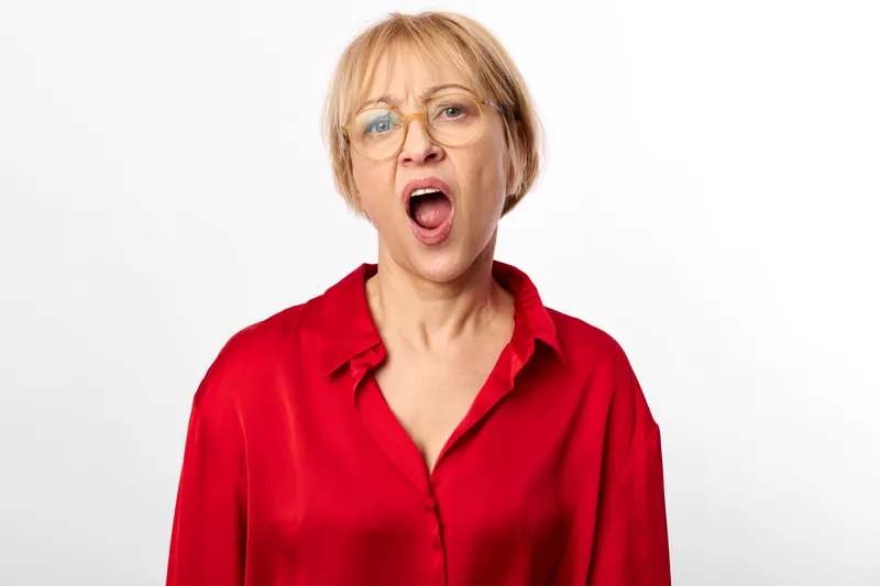 Woman surprised with open mouth, glasses and red blouse, studio portrait against white background, shocked expression, looking at camera, clean neutral studio setting