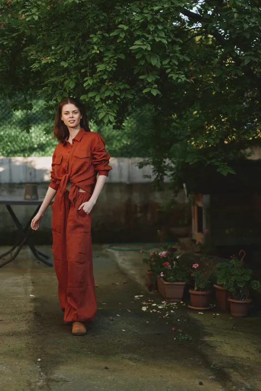 Woman in orange jumpsuit walking outdoors in a garden, natural light, candid lifestyle moment, fashion and self expression, relaxed pose, greenery and pots in the background