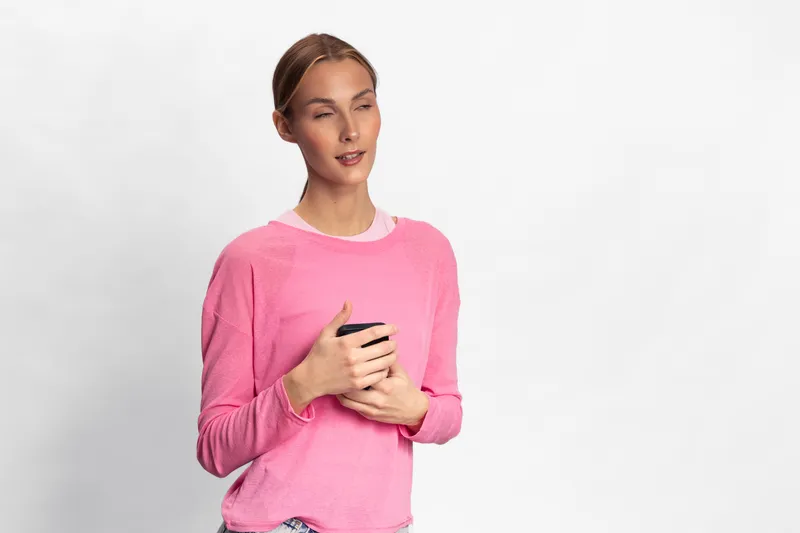 Young woman in pink sweater holds black cup with eyes closed, enjoying a quiet moment. Concept for relaxation, calm, and peaceful lifestyle with soft studio lighting.