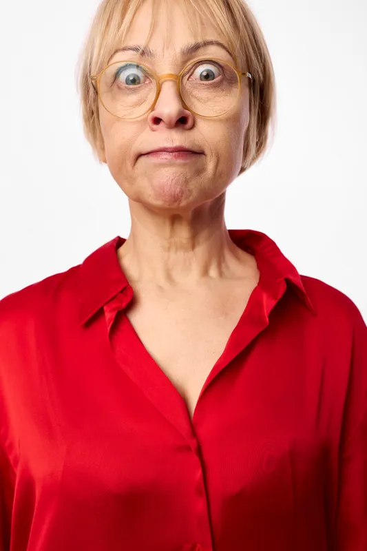 Woman with glasses, surprised worried expression, portrait in red blouse, studio lighting, neutral white background, close up headshot, direct gaze, calm tone