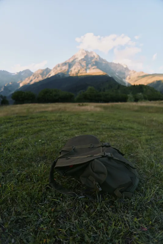 Backpack resting on a sunlit field with distant mountain range, evoking outdoor adventure, hiking, and travel lifestyle in a calm nature scene with expansive landscape.