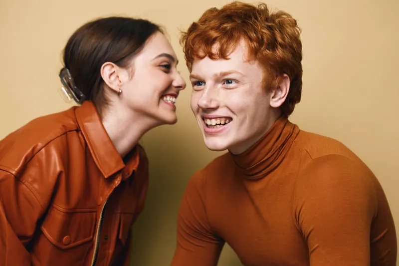 Young woman and man smiling with joy and friendship in casual autumn clothing. Closeup portrait of cheerful people enjoying conversation in warm studio environment.