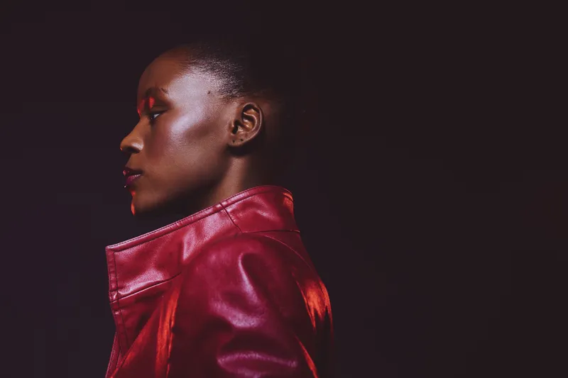 Profile of a dark skinned African woman wearing a red leather jacket against black background. Concept for fashion, style, confidence, and beauty with dramatic studio lighting.