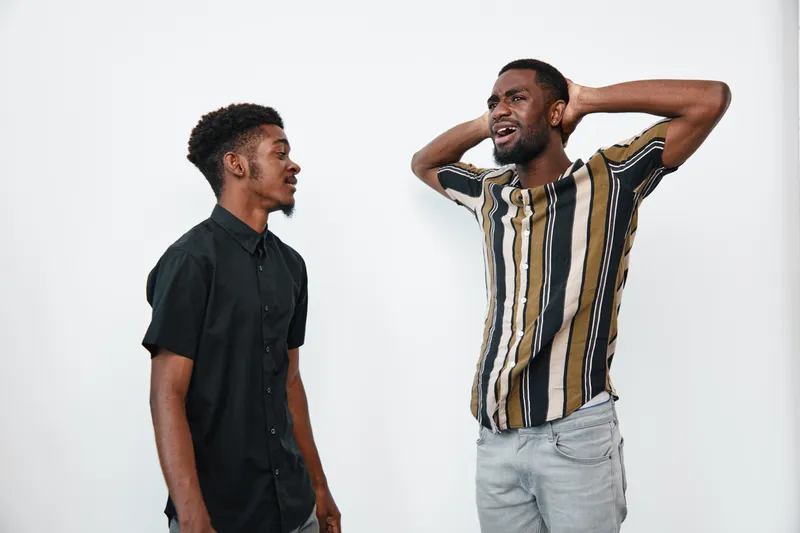 Two african american men with dark skin standing and talking on white background casual clothing and emotional expression in studio portrait.