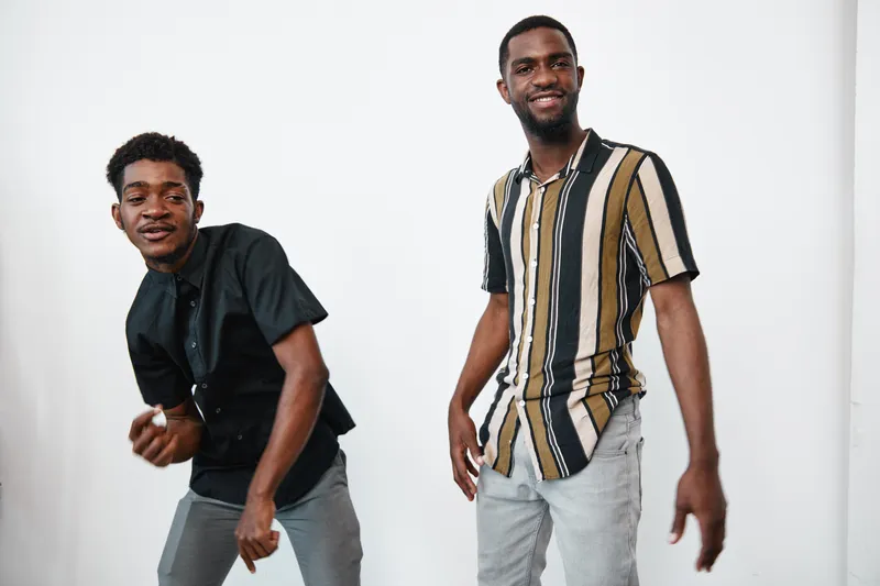 Two young black men with dark skin posing and smiling in casual clothes against white background. African ethnicity, friendship and happiness with modern style and relaxed mood.
