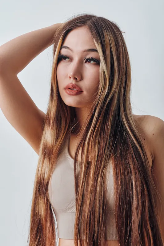 Young woman with long straight hair and natural makeup posing with hand in hair. Beauty portrait with neutral background for fashion, style, and wellness concept.